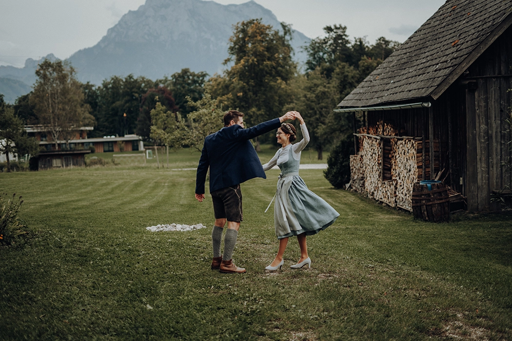 Brautpaar in Tracht tanzt in der Wiese. Bergkulisse im Hintergrund