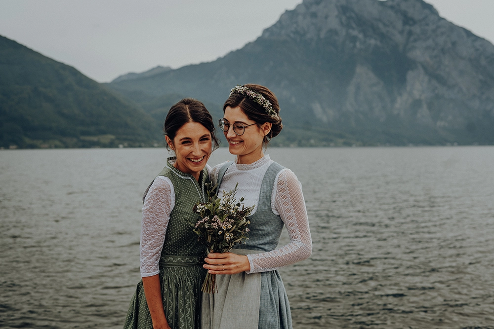 Zwei Frauen in Tracht lachen. Berg und See im Hintergrund